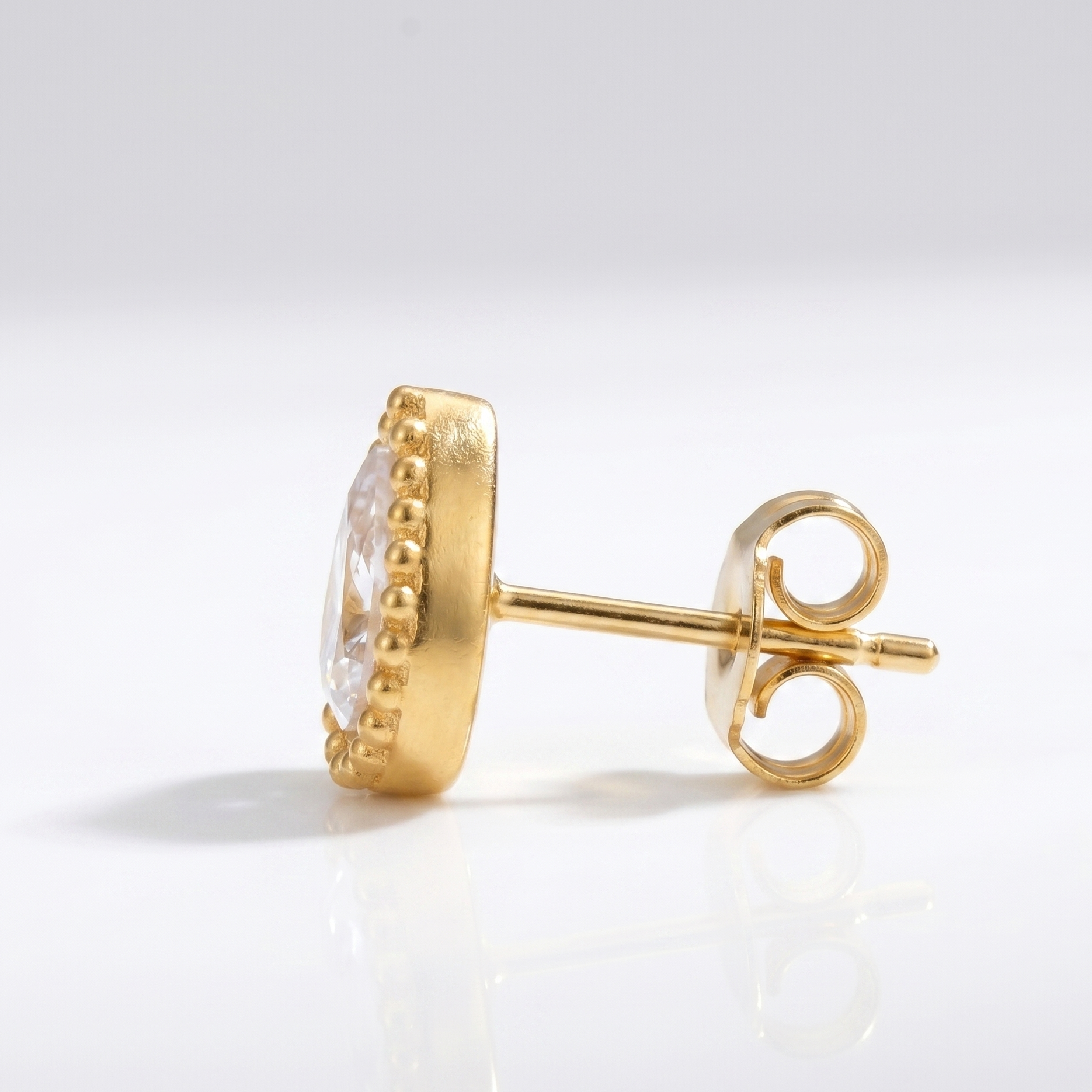 Gold earring with clear gemstone on a light gray background