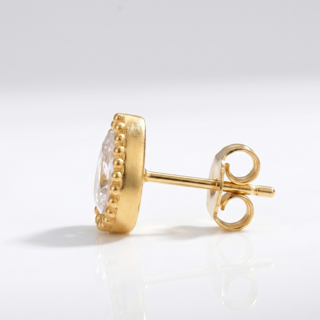 Gold earring with clear gemstone on a light gray background