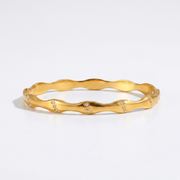 Gold bracelet with a wavy design on a light gray background