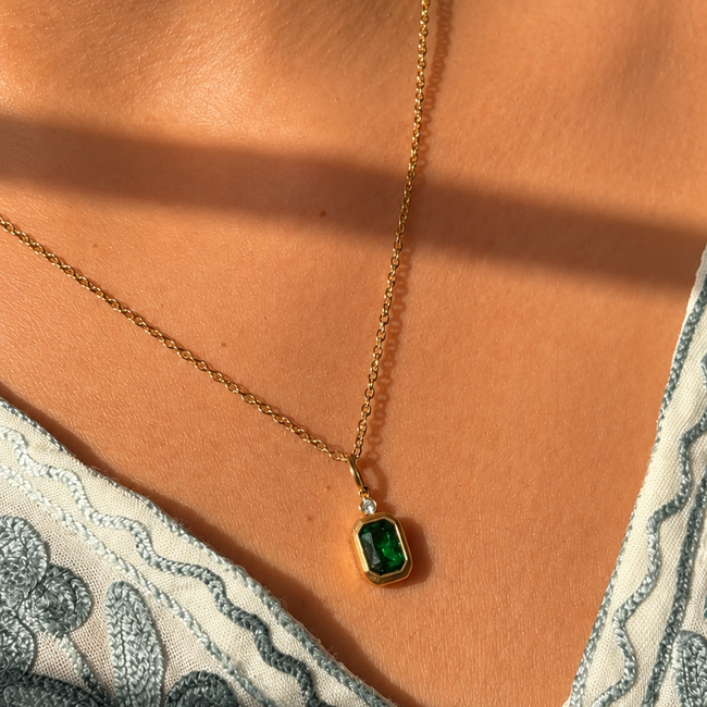 Gold necklace with a green gemstone pendant on a person wearing a patterned garment.