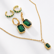 Gold jewelry set with emerald green gemstones on a white background