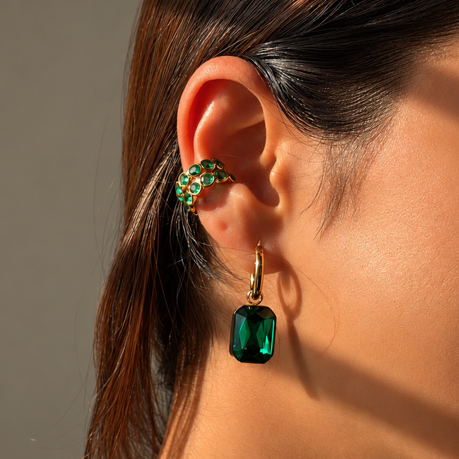 Close-up of a person wearing green gemstone earrings with a neutral background
