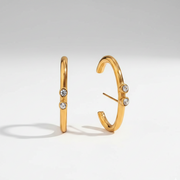 It Girl Earrings revealing the durable anti-tarnish gold finish and modern C-shaped wrap structure accented with clear crystals.