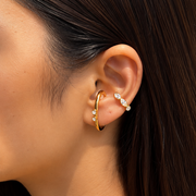 Close-up of a person wearing gold hoop earrings with small pearls.